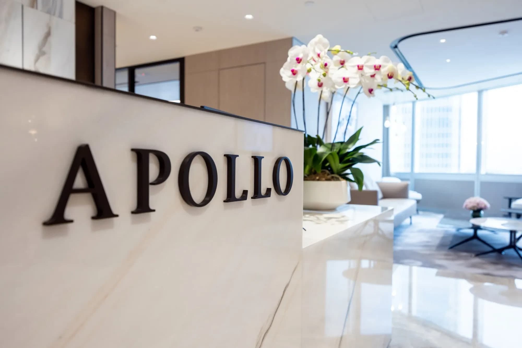 The Apollo logo on a marble reception desk in a modern office lobby, with white orchids and seating visible in the background