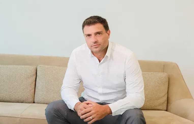 Pablo Marcelo Barreiro seated on a beige sofa in a white button up shirt, hands clasped, looking at the camera