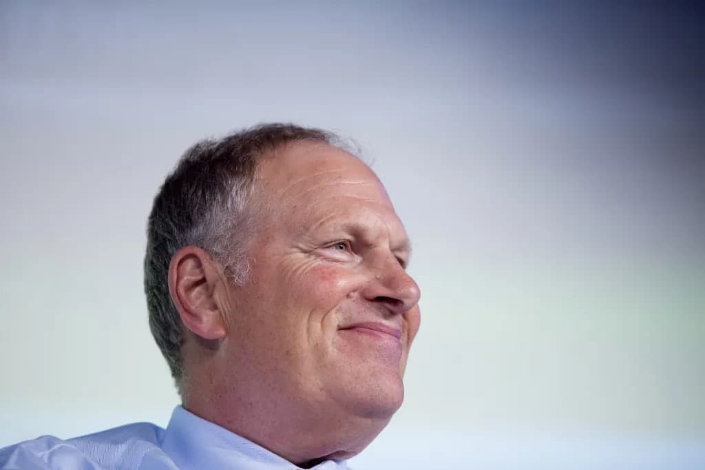 David Cote smiling and looking off camera, wearing a light blue button up shirt, photographed against a softly lit gradient background