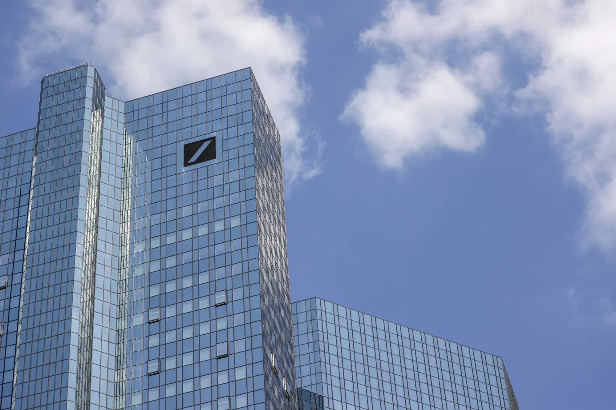 A low angle view of the Deutsche Bank headquarters tower in Frankfurt with its logo on the glass facade against a blue sky