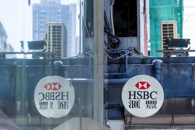 HSBC signage reflected in glass on an office building exterior in Hong Kong, with the bank's red and white logo visible on two circular signs