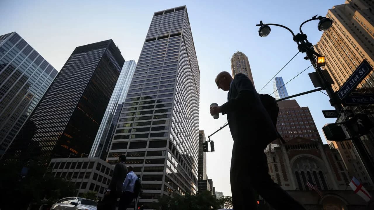 A businessman silhouetted against the sky walking through a Manhattan intersection with skyscrapers in the background